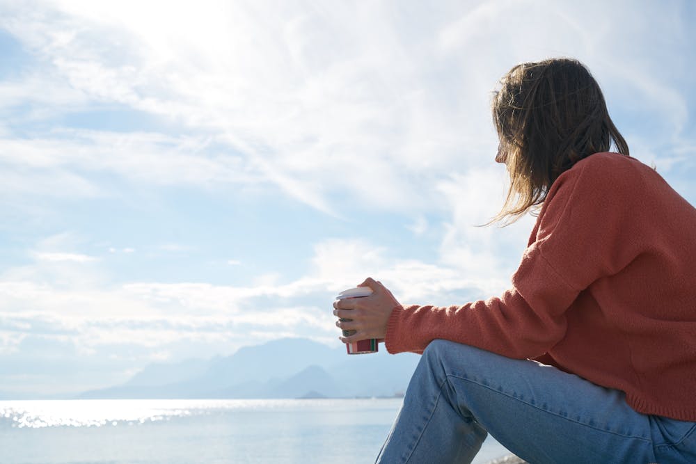 Woman sitting and contemplating in front of a body of water.