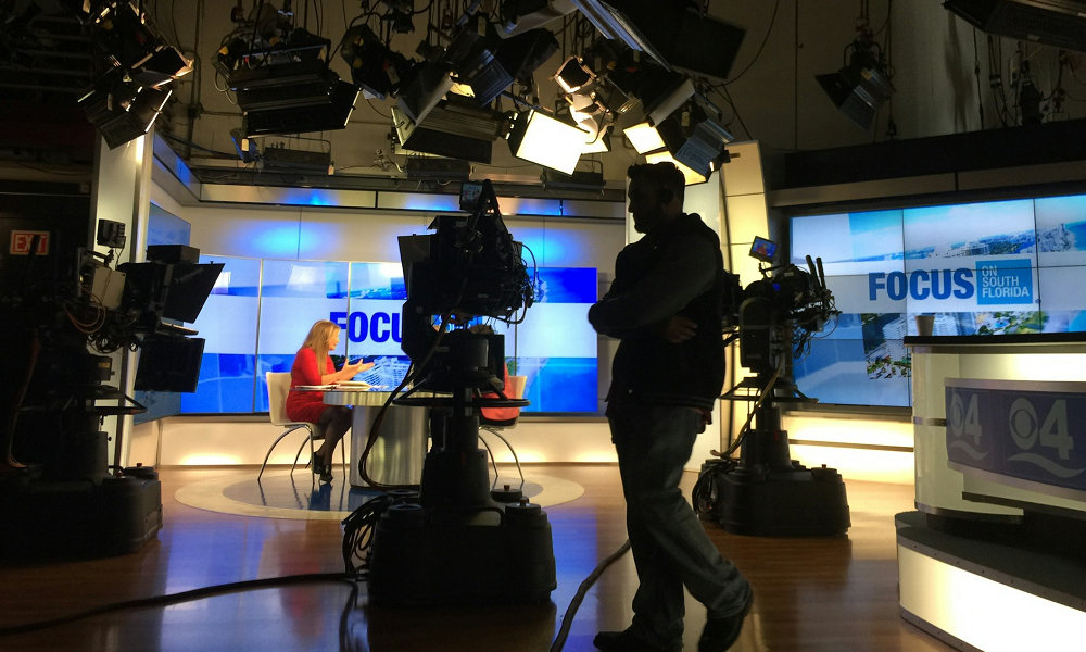 A TV news studio, with cameras, lighting, staff, and a host.